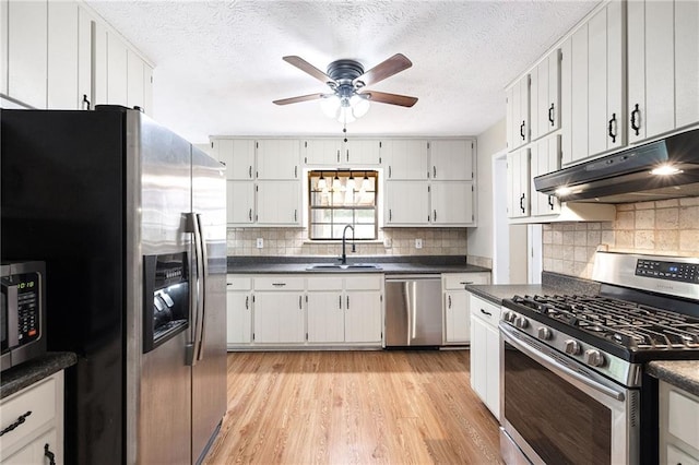 kitchen featuring a ceiling fan, under cabinet range hood, a sink, dark countertops, and appliances with stainless steel finishes