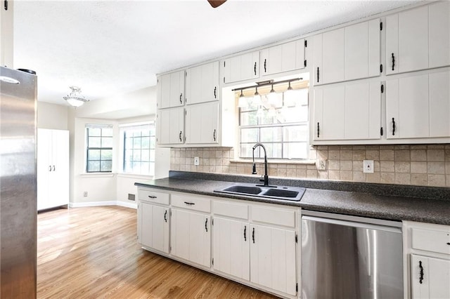 kitchen featuring light wood-style flooring, baseboards, a sink, dark countertops, and appliances with stainless steel finishes