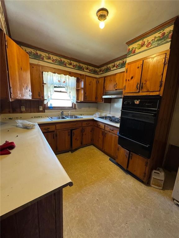 kitchen featuring a warming drawer, light floors, brown cabinetry, a sink, and oven