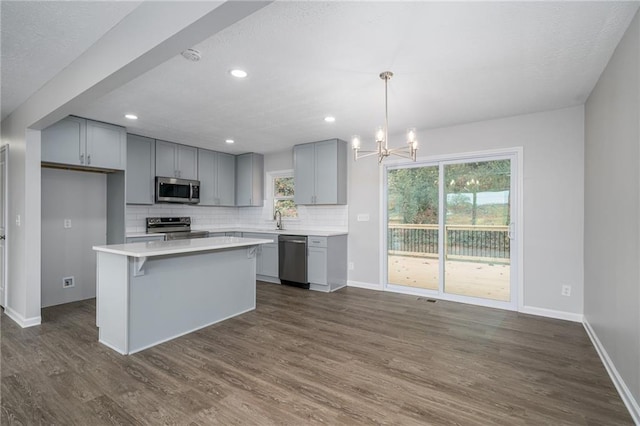 kitchen featuring a center island, hanging light fixtures, stainless steel appliances, gray cabinets, and decorative backsplash