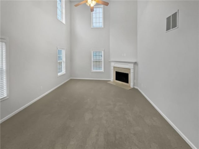 unfurnished living room featuring ceiling fan, a towering ceiling, and carpet