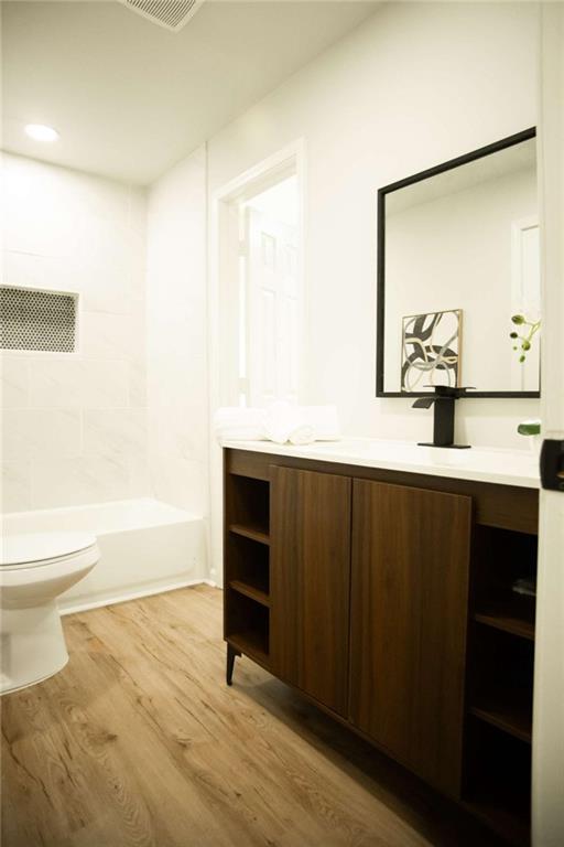 full bathroom featuring washtub / shower combination, hardwood / wood-style floors, toilet, and vanity