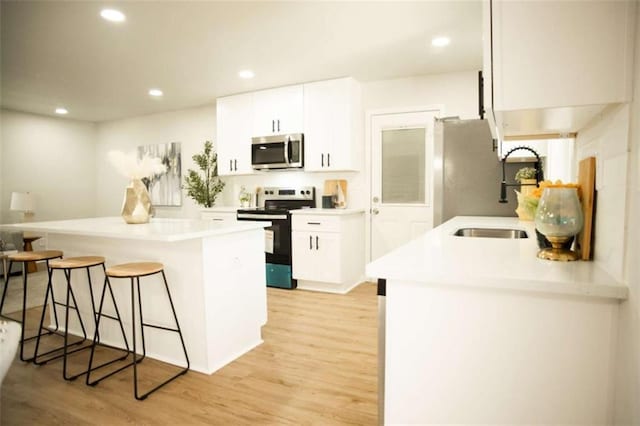 kitchen featuring white cabinets, a kitchen bar, stainless steel appliances, and light hardwood / wood-style flooring