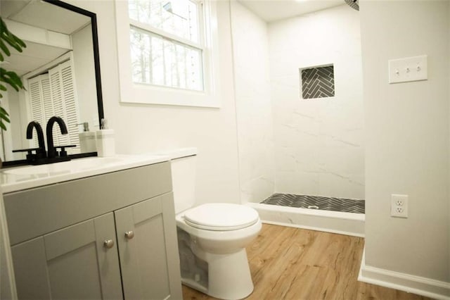 bathroom with toilet, vanity, wood-type flooring, and a tile shower