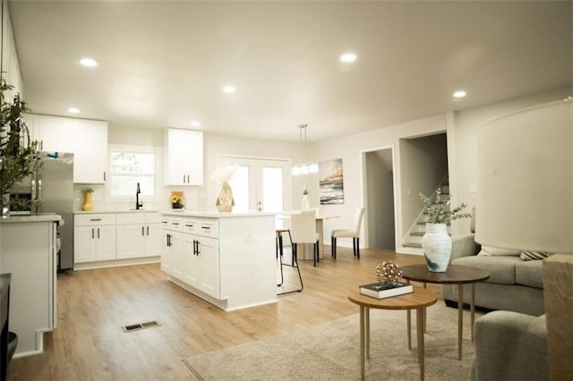 kitchen with pendant lighting, a kitchen island, light wood-type flooring, white cabinets, and stainless steel fridge