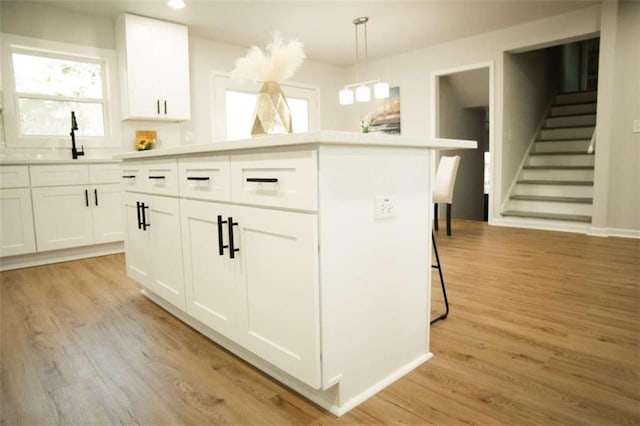 kitchen with pendant lighting, white cabinets, light wood-type flooring, and a kitchen island