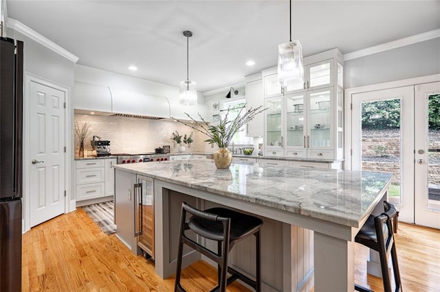 kitchen with a breakfast bar area, plenty of natural light, white cabinetry, light wood-type flooring, and ornamental molding