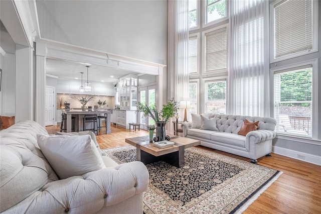 living area with a high ceiling, light wood-style floors, and baseboards