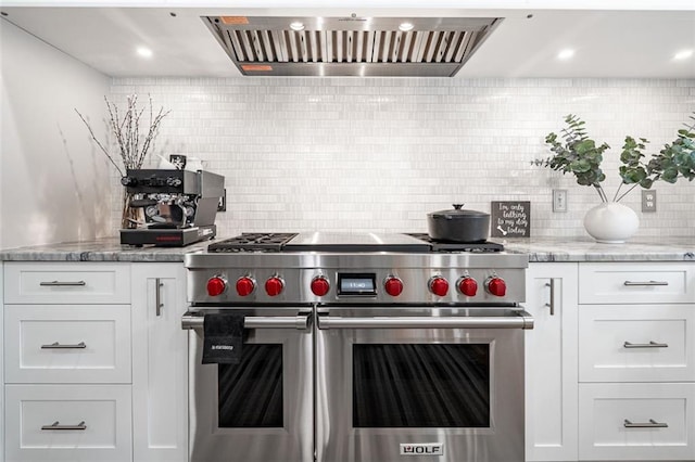 kitchen featuring range with two ovens, custom range hood, decorative backsplash, white cabinets, and light stone counters