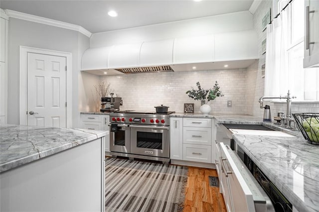 kitchen with double oven range, a sink, white cabinetry, light wood-type flooring, and ornamental molding