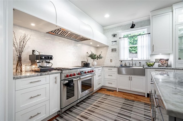 kitchen with range with two ovens, a sink, decorative backsplash, and white cabinetry