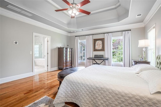 bedroom featuring wood finished floors, a tray ceiling, baseboards, ornamental molding, and ensuite bathroom