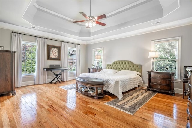 bedroom featuring a raised ceiling, ornamental molding, multiple windows, and light wood-style flooring