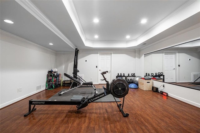 workout area featuring ornamental molding, a raised ceiling, wood finished floors, recessed lighting, and baseboards