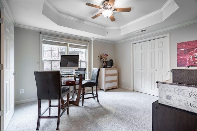 office area featuring a tray ceiling, light colored carpet, crown molding, a ceiling fan, and baseboards