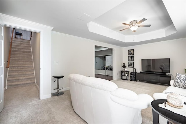 living area featuring light colored carpet, ceiling fan, a tray ceiling, stairway, and baseboards