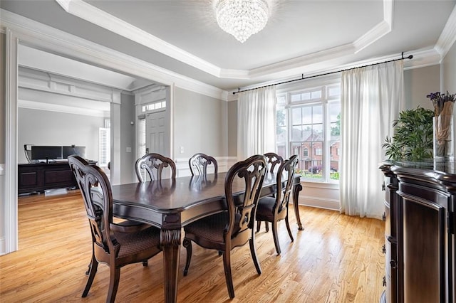 dining space with a chandelier, crown molding, a tray ceiling, and light wood-style floors