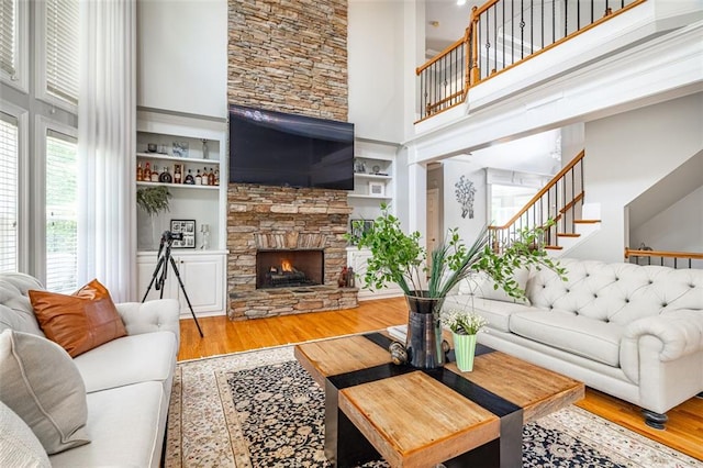 living room with a towering ceiling, wood finished floors, stairs, and a stone fireplace