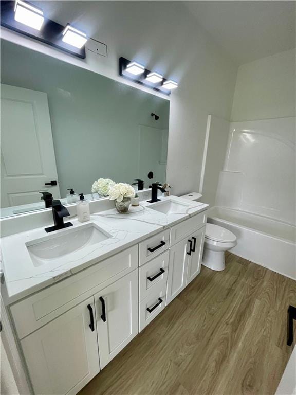 bathroom featuring double vanity, toilet, a sink, and wood finished floors