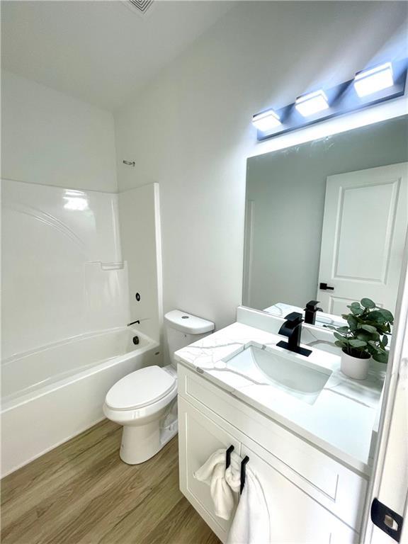 bathroom featuring toilet, shower / bath combination, wood finished floors, and vanity