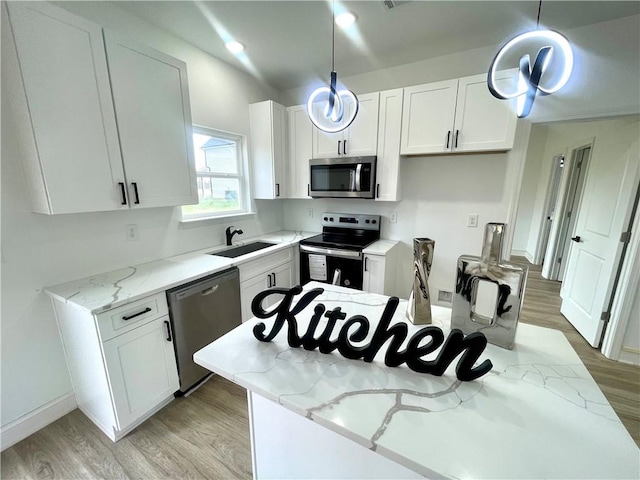 kitchen featuring appliances with stainless steel finishes, a sink, light stone counters, light wood finished floors, and white cabinetry