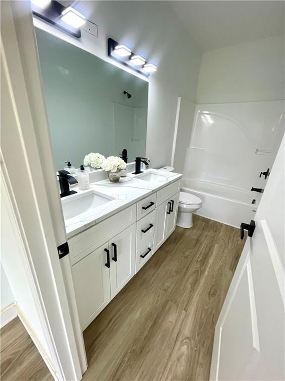 bathroom with double vanity, toilet, wood finished floors, and a sink