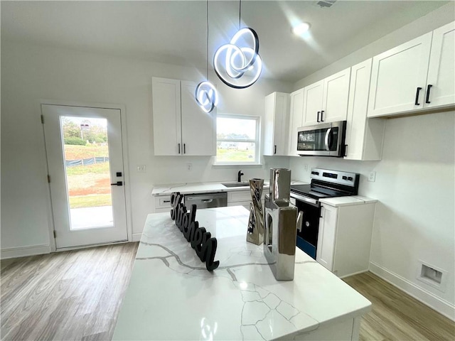 kitchen featuring light wood-style floors, white cabinetry, light stone counters, appliances with stainless steel finishes, and hanging light fixtures