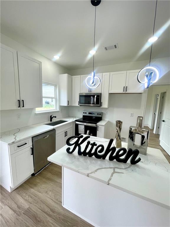 kitchen with a sink, light wood-style flooring, white cabinets, and stainless steel appliances