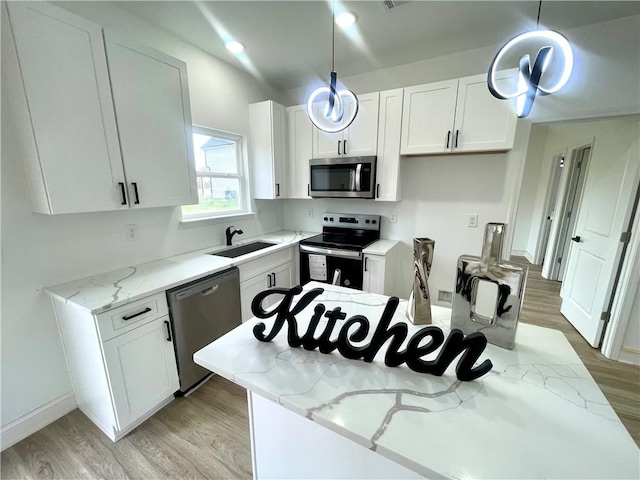 kitchen featuring white cabinets, light stone countertops, appliances with stainless steel finishes, a sink, and light wood-type flooring