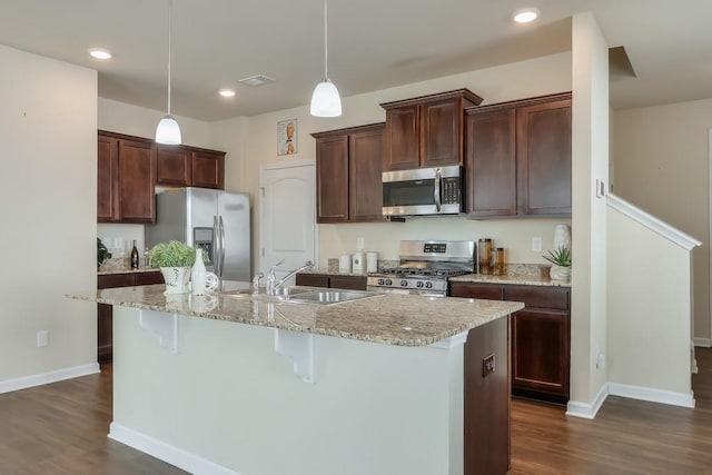 kitchen with appliances with stainless steel finishes, a sink, hanging light fixtures, and a center island with sink