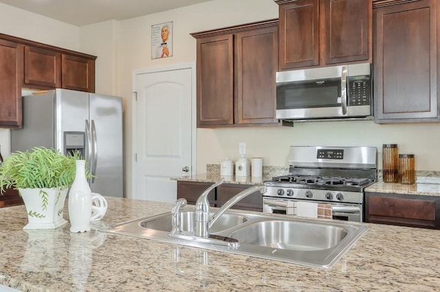 kitchen featuring stainless steel appliances, a sink, and light stone countertops