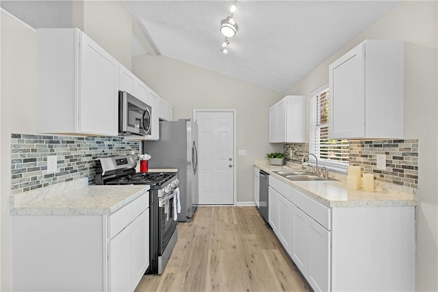 kitchen with vaulted ceiling, light countertops, a sink, appliances with stainless steel finishes, and white cabinets