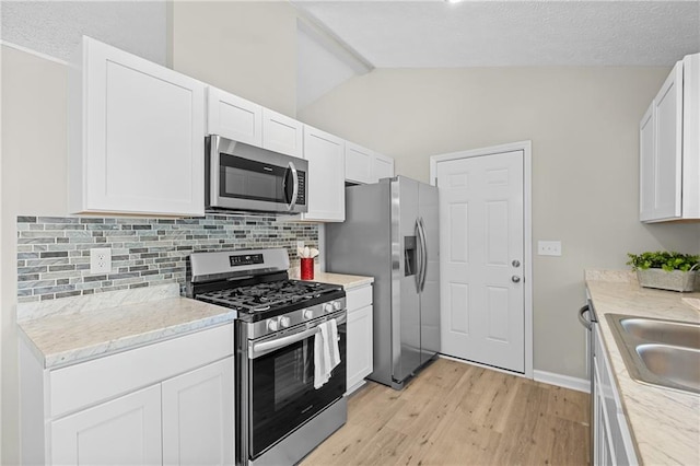 kitchen featuring vaulted ceiling, white cabinetry, light wood-style flooring, stainless steel appliances, and decorative backsplash