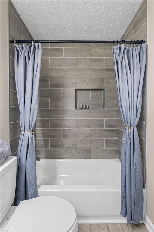 full bathroom with toilet, shower / bath combination with curtain, and a textured ceiling