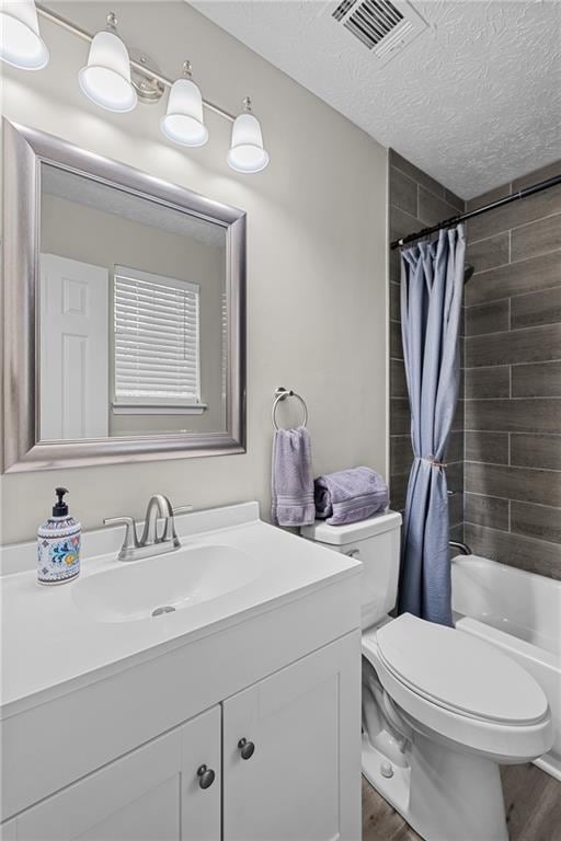 full bath featuring vanity, toilet, a textured ceiling, visible vents, and wood finished floors