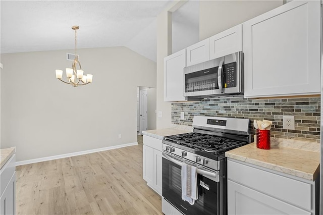 kitchen featuring white cabinets, stainless steel appliances, tasteful backsplash, lofted ceiling, and a notable chandelier