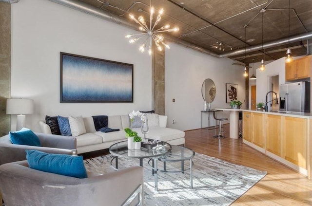 living room with an inviting chandelier, sink, a towering ceiling, and light wood-type flooring