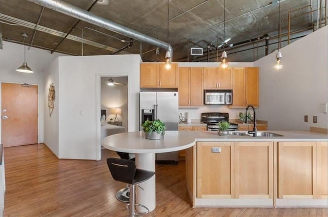 kitchen featuring light wood-style flooring, stainless steel appliances, a sink, hanging light fixtures, and light countertops