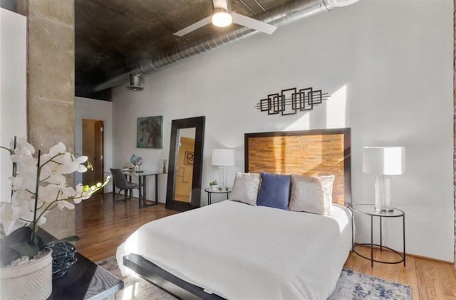 bedroom with ceiling fan, wood finished floors, and a towering ceiling