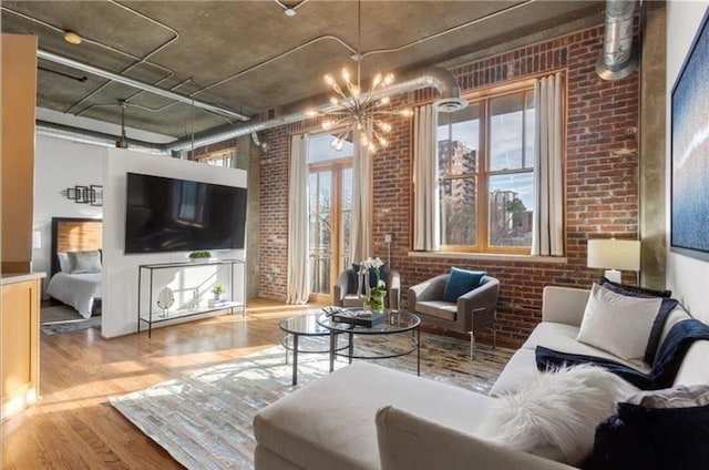 living room with a notable chandelier, brick wall, and wood finished floors