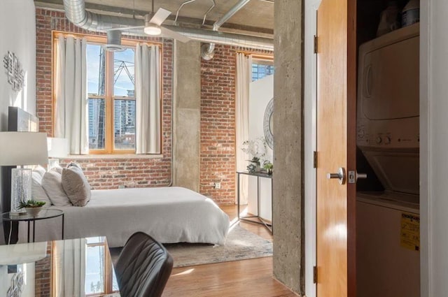 bedroom with stacked washer / dryer, multiple windows, brick wall, and wood finished floors