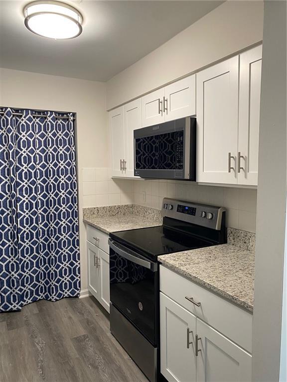 kitchen with dark hardwood / wood-style flooring, white cabinetry, stainless steel appliances, and tasteful backsplash