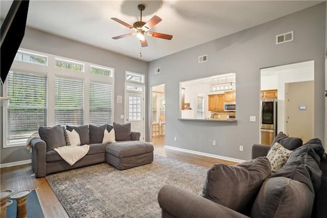 living room featuring visible vents, light wood-type flooring, a ceiling fan, and baseboards
