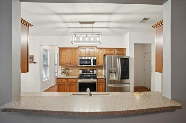 kitchen with visible vents, a peninsula, light stone countertops, backsplash, and stainless steel appliances