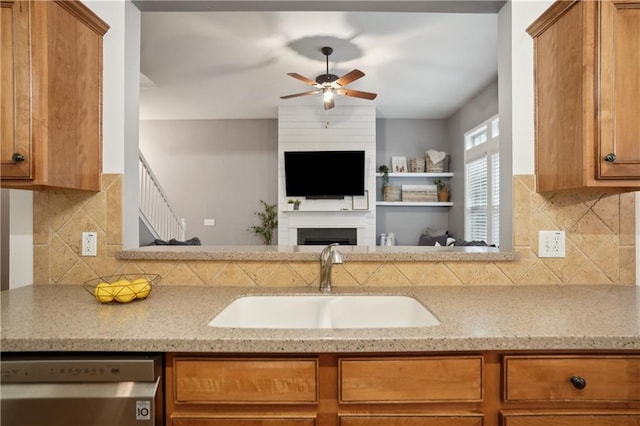 kitchen with dishwasher, a sink, ceiling fan, brown cabinets, and light stone countertops