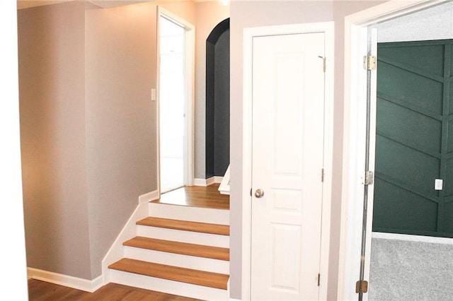 stairway with arched walkways, baseboards, and wood finished floors
