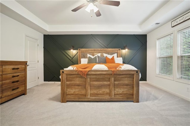 bedroom featuring visible vents, baseboards, a ceiling fan, a tray ceiling, and light colored carpet