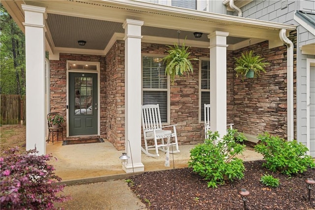property entrance featuring covered porch, fence, and stone siding