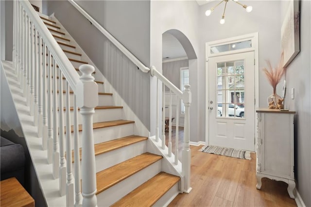foyer entrance featuring baseboards, stairway, a high ceiling, arched walkways, and wood finished floors