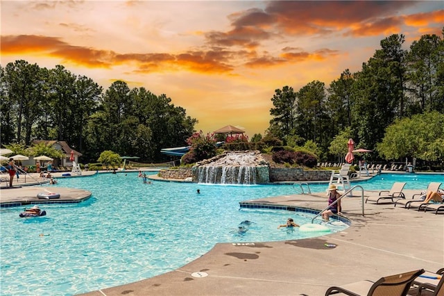 pool at dusk featuring a patio and a community pool
